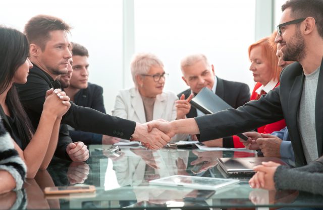 business, technology and office concept - two smiling businessman shaking hands in office